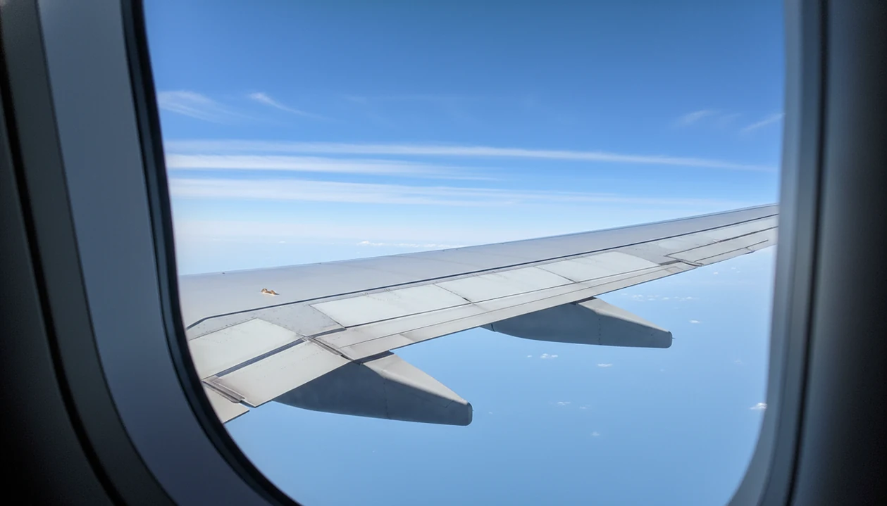 An airplane wing crosses a clear blue sky, suggesting invisible turbulence at cruising altitude.